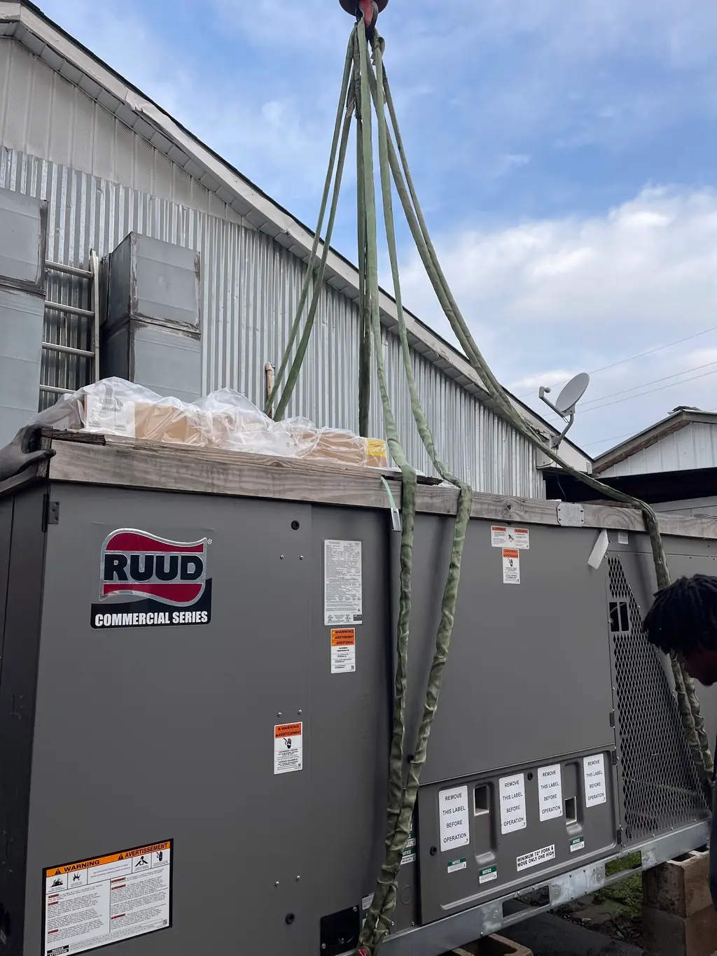 A RUUD Commercial Series packaged unit on crane slings at ground level before being lifted to the roof