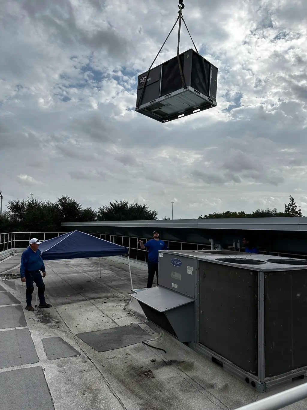 A RUUD packaged rooftop unit on a crane sling above an Aaron Mechanical crew